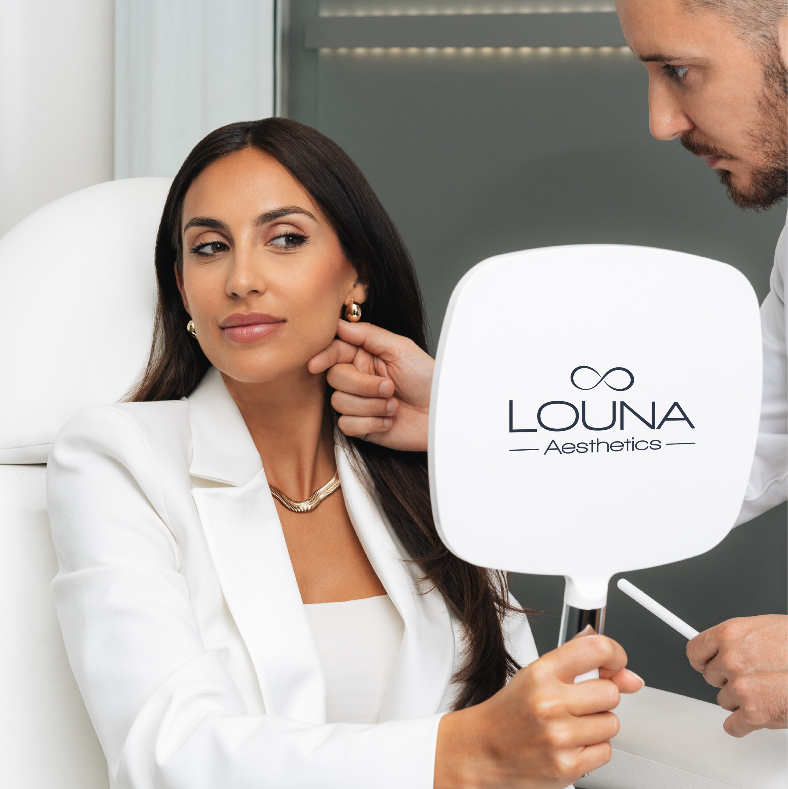 Female patient examining aesthetic results in mirror branded with Louna Aesthetics
