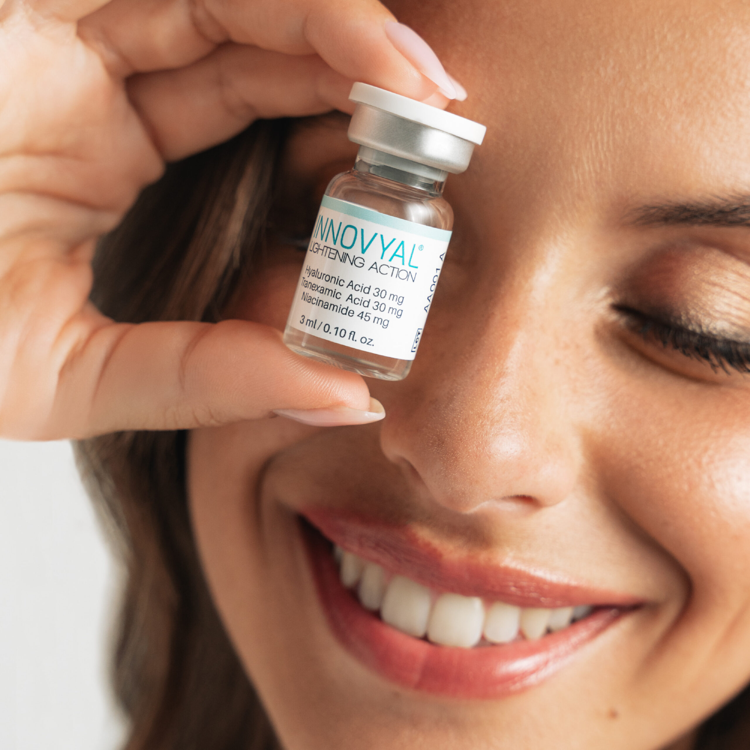 Smiling woman holding INNOVYAL dermobooster vial, promoting confidence and product use